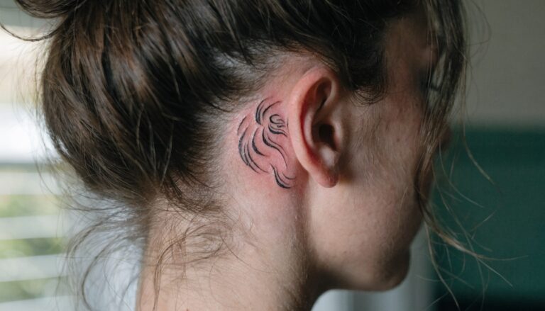 Minimal black linework tiger head tattoo behind a woman's ear on the side of her neck