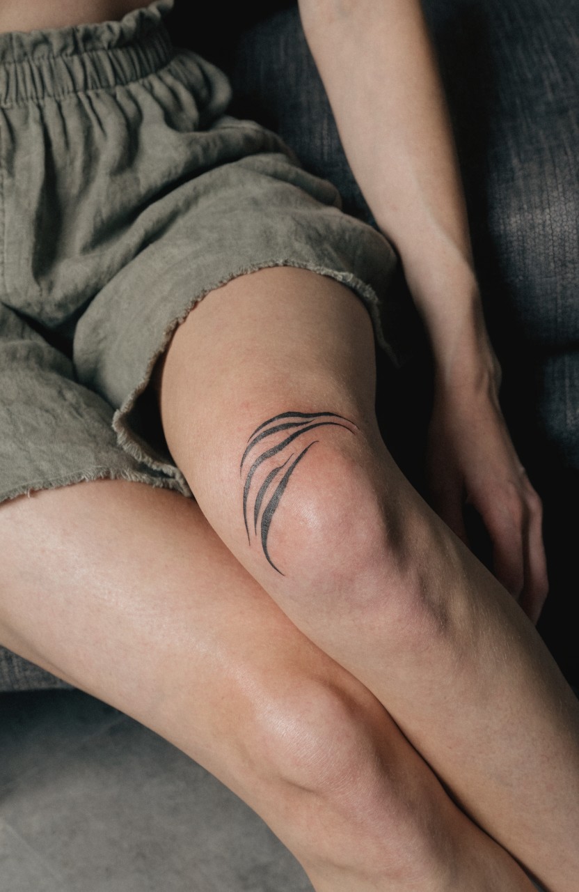 Minimal black line tiger stripes tattoo wrapping a woman's knee