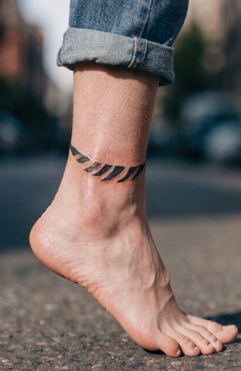 Woman's ankle with minimalist black tiger stripe band tattoo wrapping as an anklet