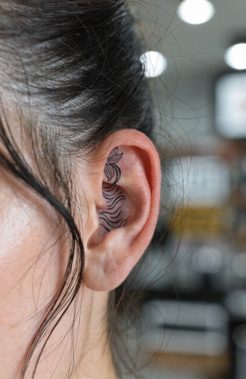 Woman's ear tattooed with fine line black tiger stripes wrapping the outer cartilage