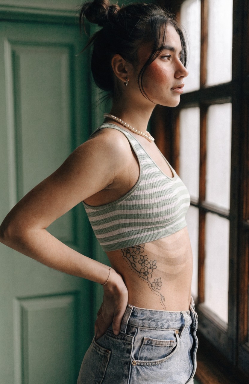 Delicate black floral vine tattoo trailing down a woman's side torso over her ribcage