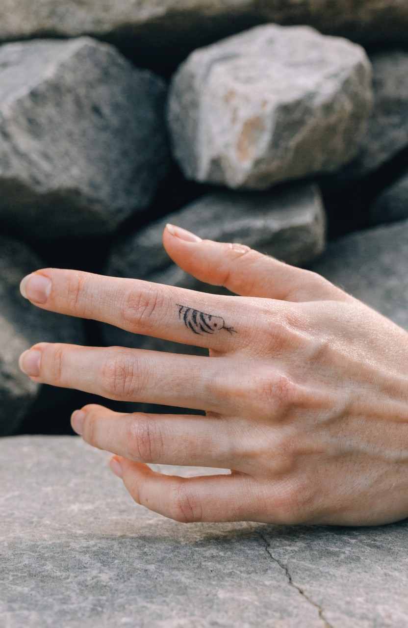 Small black line tiger stripe tattoo on the side of a woman's index finger resting on rocks