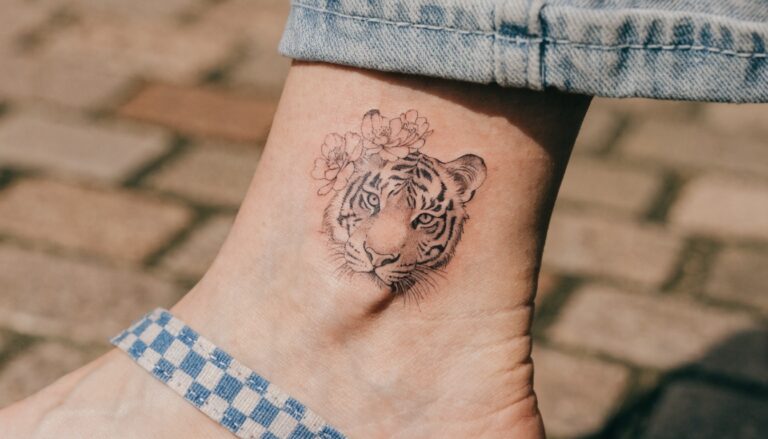 19 Beautiful Tiger and Flowers Tattoo Ideas for a Soft Yet Fierce Look Fine line black ink tattoo of tiger face and peony flower on side of ankle over tiled ground