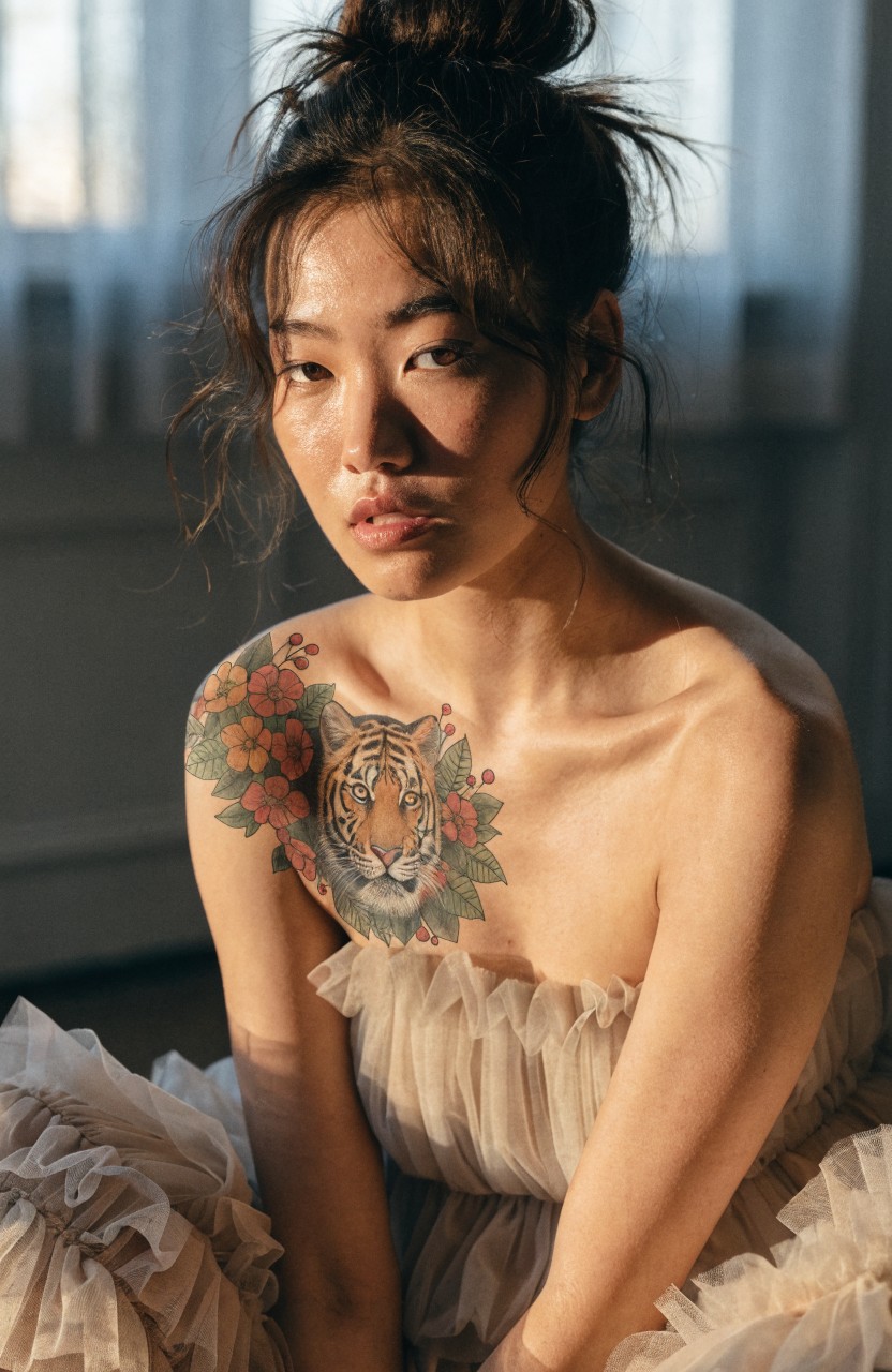Colorful tiger head tattoo with surrounding flowers on a woman's shoulder and upper chest