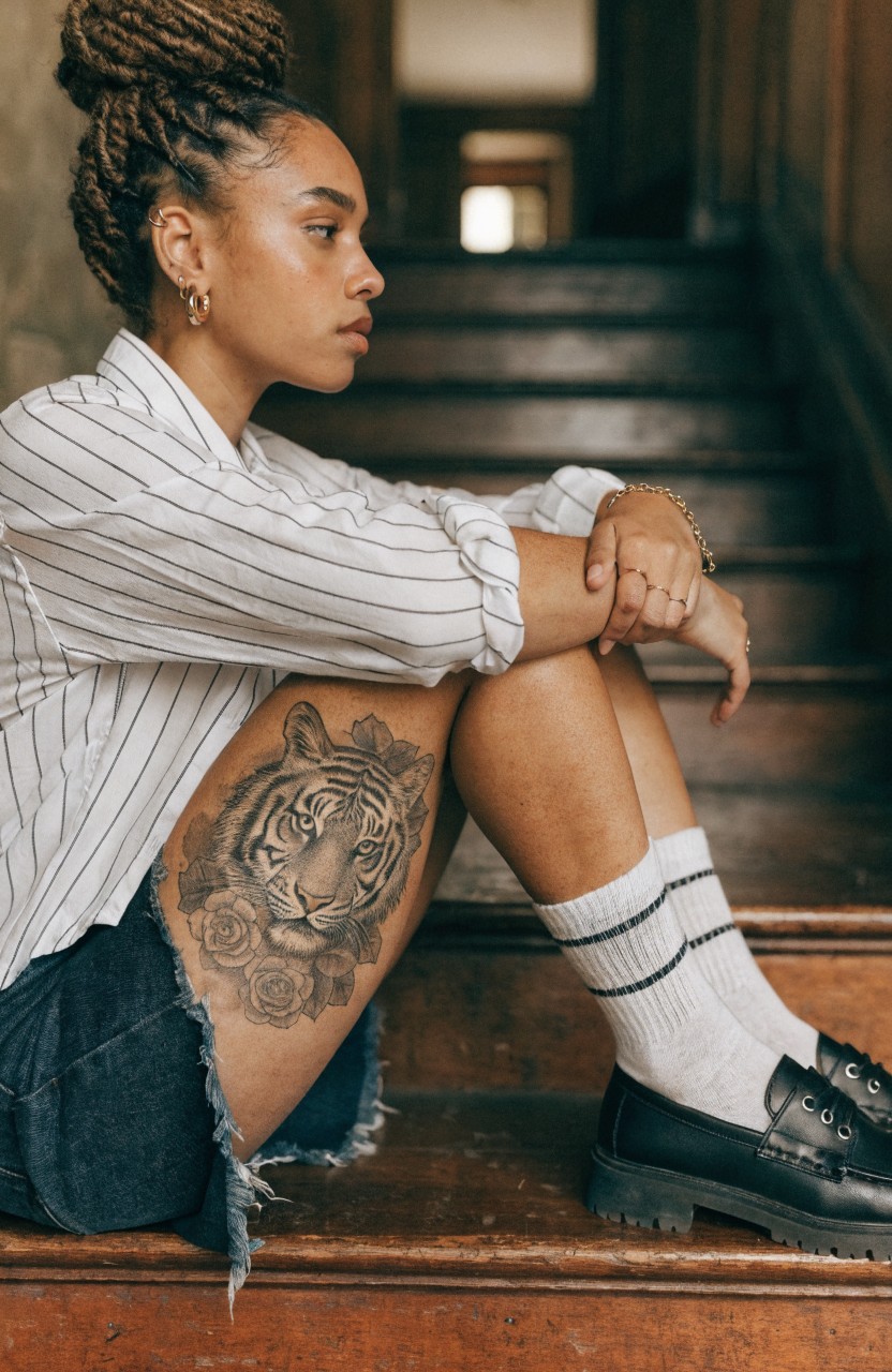 Black and grey tiger head tattoo with surrounding roses on a woman's upper thigh