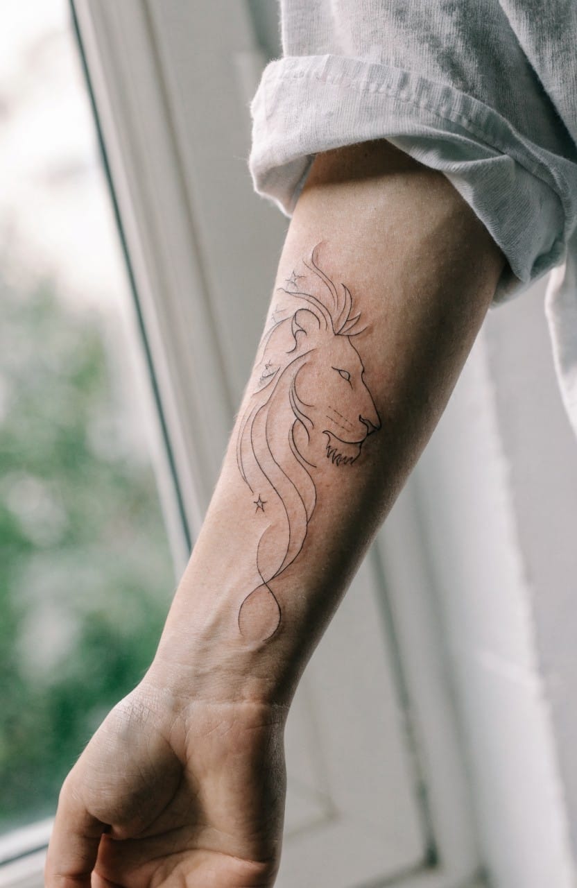 Minimalist black linework lion profile tattoo on inner forearm with swirling mane lines and star detail
