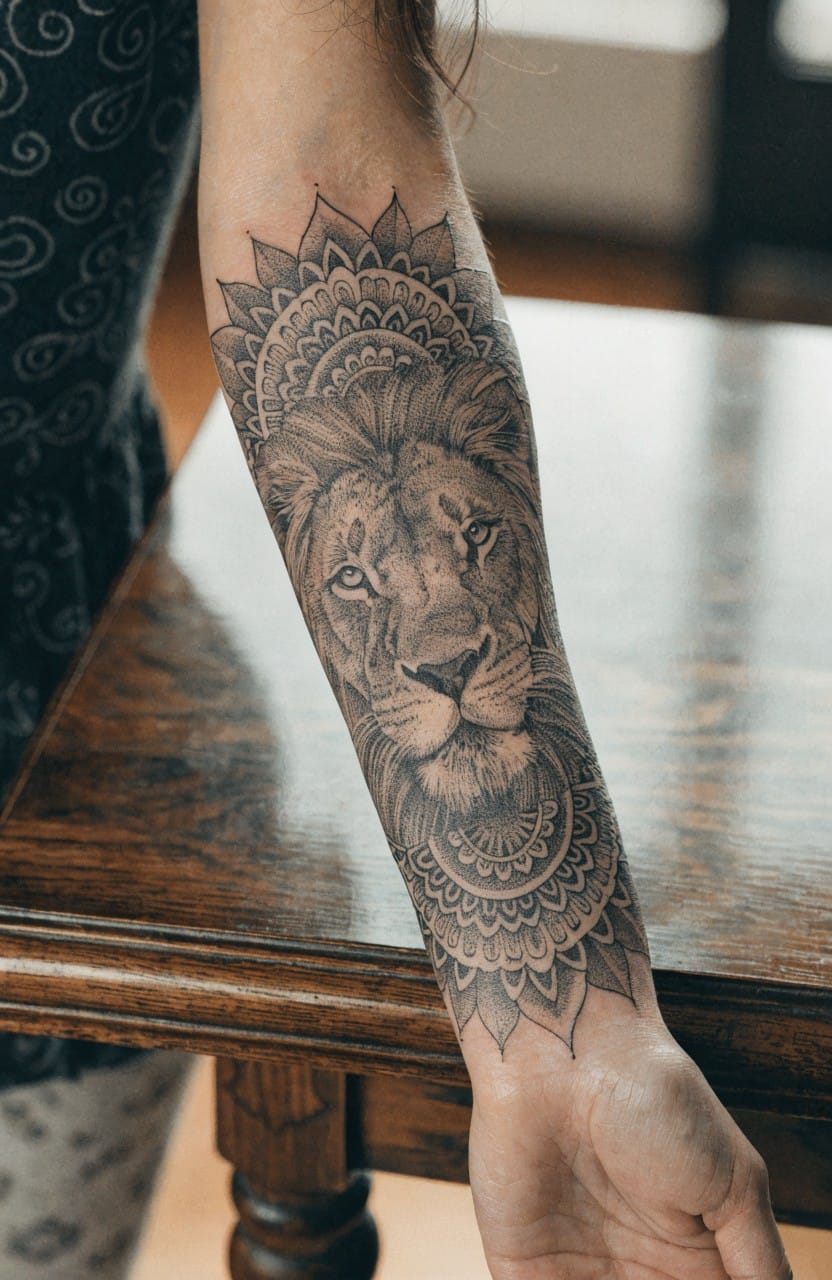 Black and grey lion head tattoo with intricate mandala patterns forming a forearm sleeve on a woman's arm
