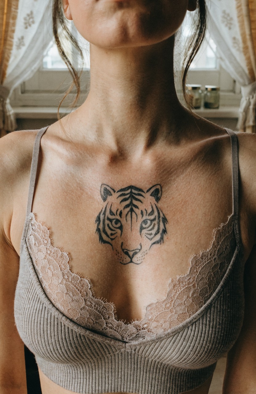 Black linework tiger face tattoo centered on a woman's upper chest over gray lace bralette