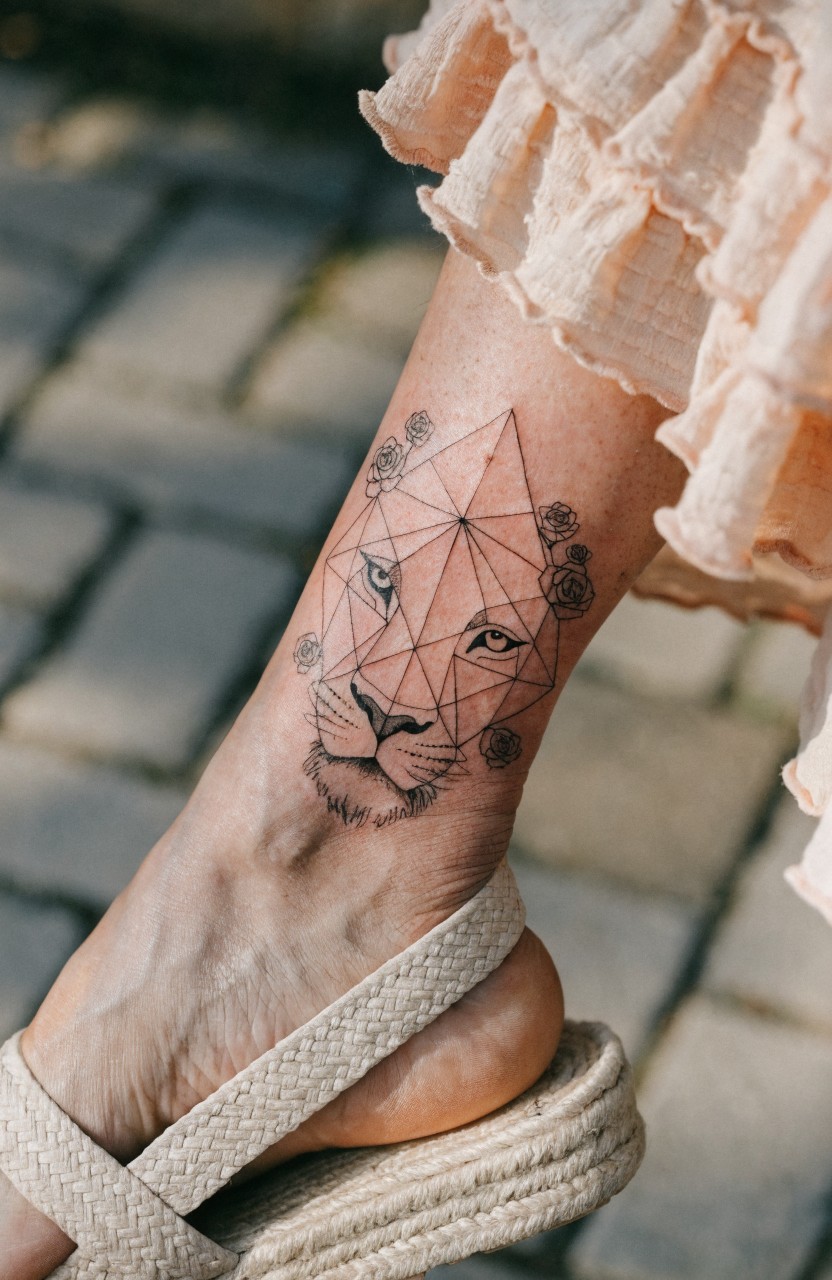Geometric linework lion head with roses tattooed on the side of a woman's lower leg above the ankle