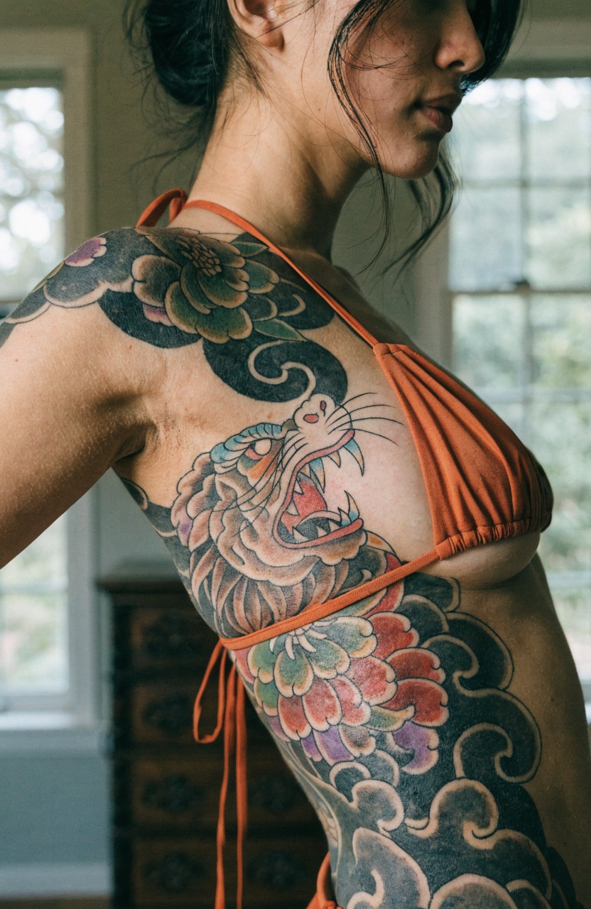 Woman's side torso with large traditional Japanese tattoo featuring snarling tiger head surrounded by colorful peonies and swirling waves