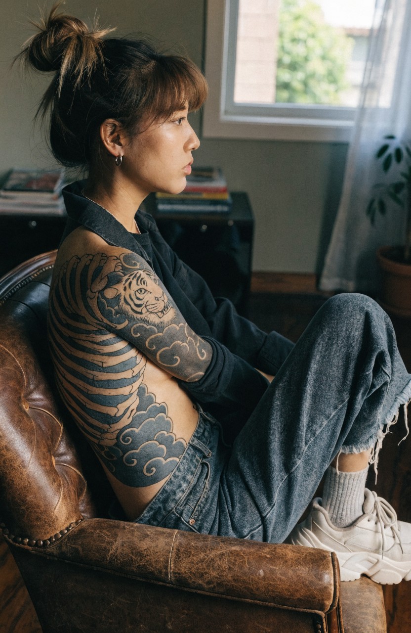 Woman seated showing large black and gray Japanese tiger tattoo wrapping her side torso with clouds and stripes