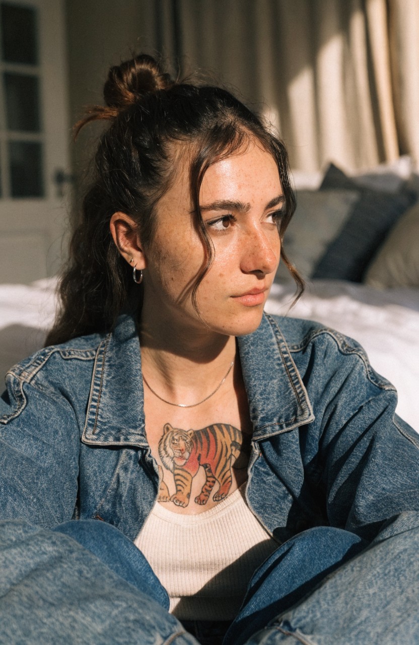 Colorful realistic tiger tattoo on woman's upper chest visible under open denim jacket