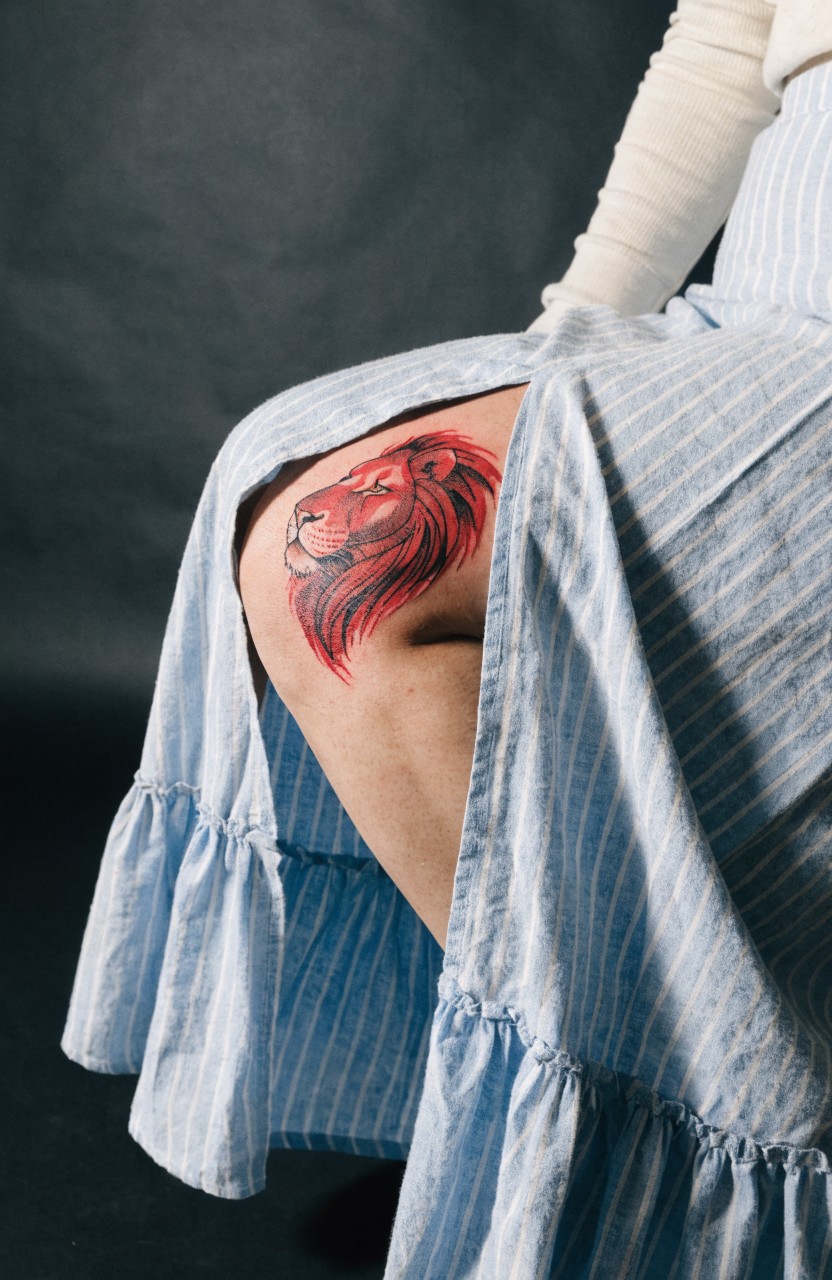 Red lion head tattoo on outer thigh with flowing mane and detailed shading curving along the leg