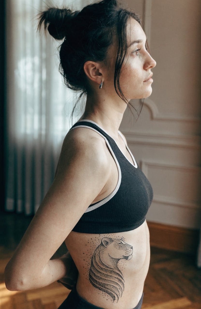 Black and grey lion tattoo in profile on woman's side torso with shaded flowing mane