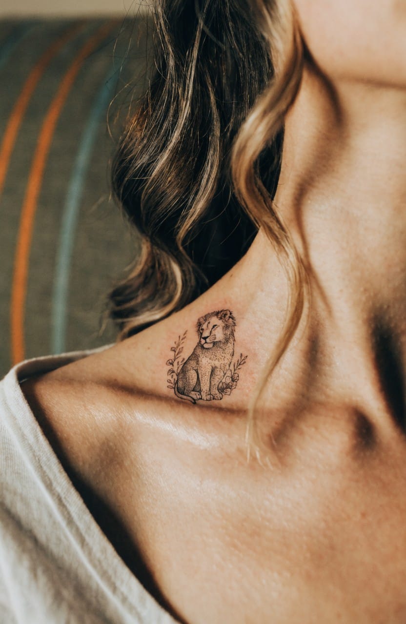 Delicate fine line tattoo of a small lion cub with subtle floral details on a woman's upper shoulder