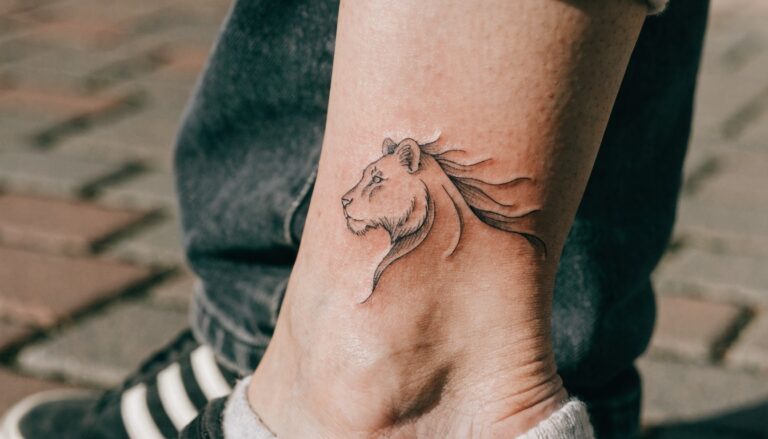 23 Beautiful Lion Tattoo Ideas for Women Worth Saving Minimalist black linework lion tattoo on a woman's ankle and lower leg with subtle shading on a shiny skin surface