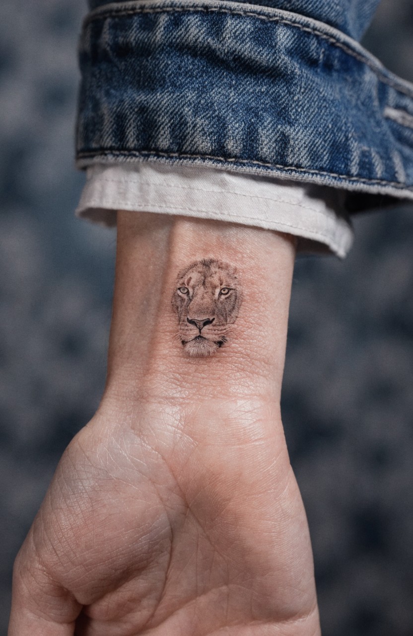 Small fine line lion head tattoo with subtle shading on a woman's inner wrist