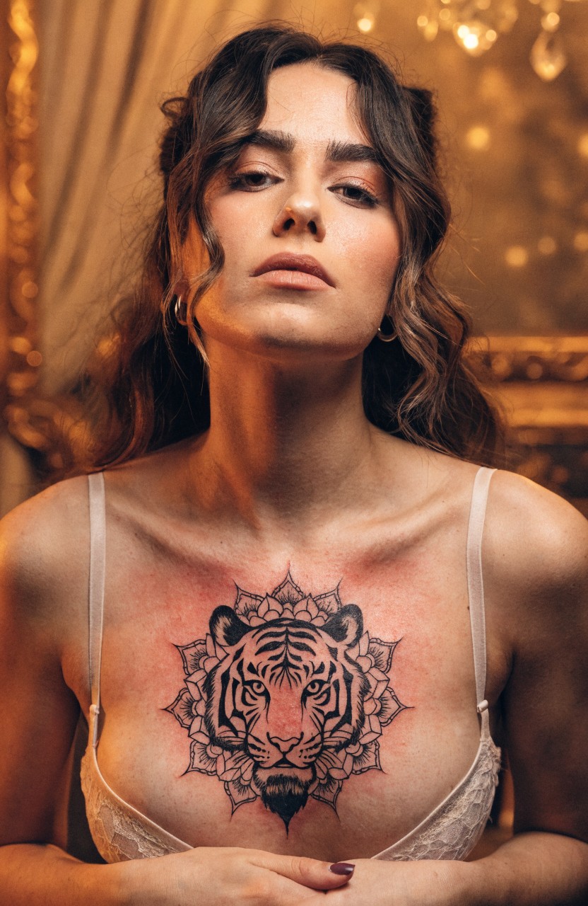 Closeup portrait of woman with large black ink mandala tiger tattoo across upper chest, intricate linework blending tiger face and floral patterns, white lace bra visible