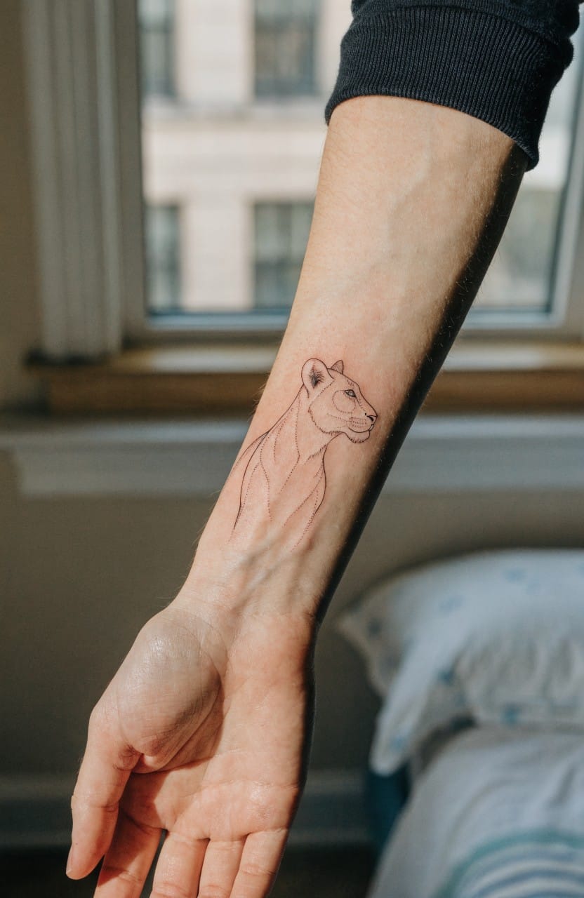 Fine line black ink lioness profile tattoo on a woman's inner forearm