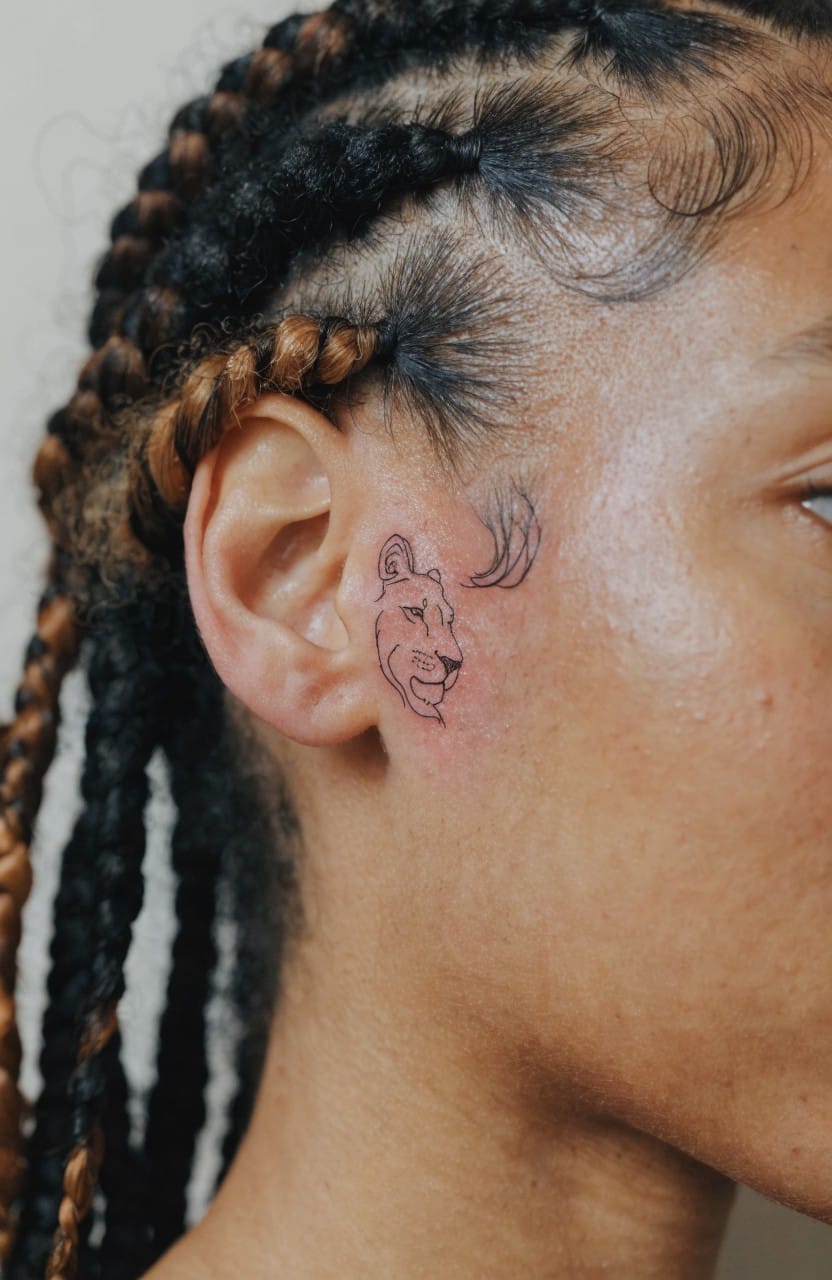 Woman's profile with small fine-line lioness head tattoo near her ear on the side of her face