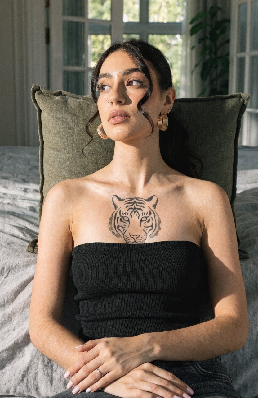 Symmetrical fine line tiger head tattoo on upper chest with intense eyes and whisker details in black ink