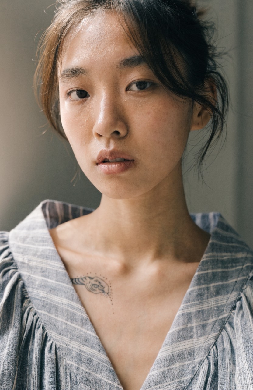 Delicate fine line tiger head tattoo on collarbone above striped blouse neckline