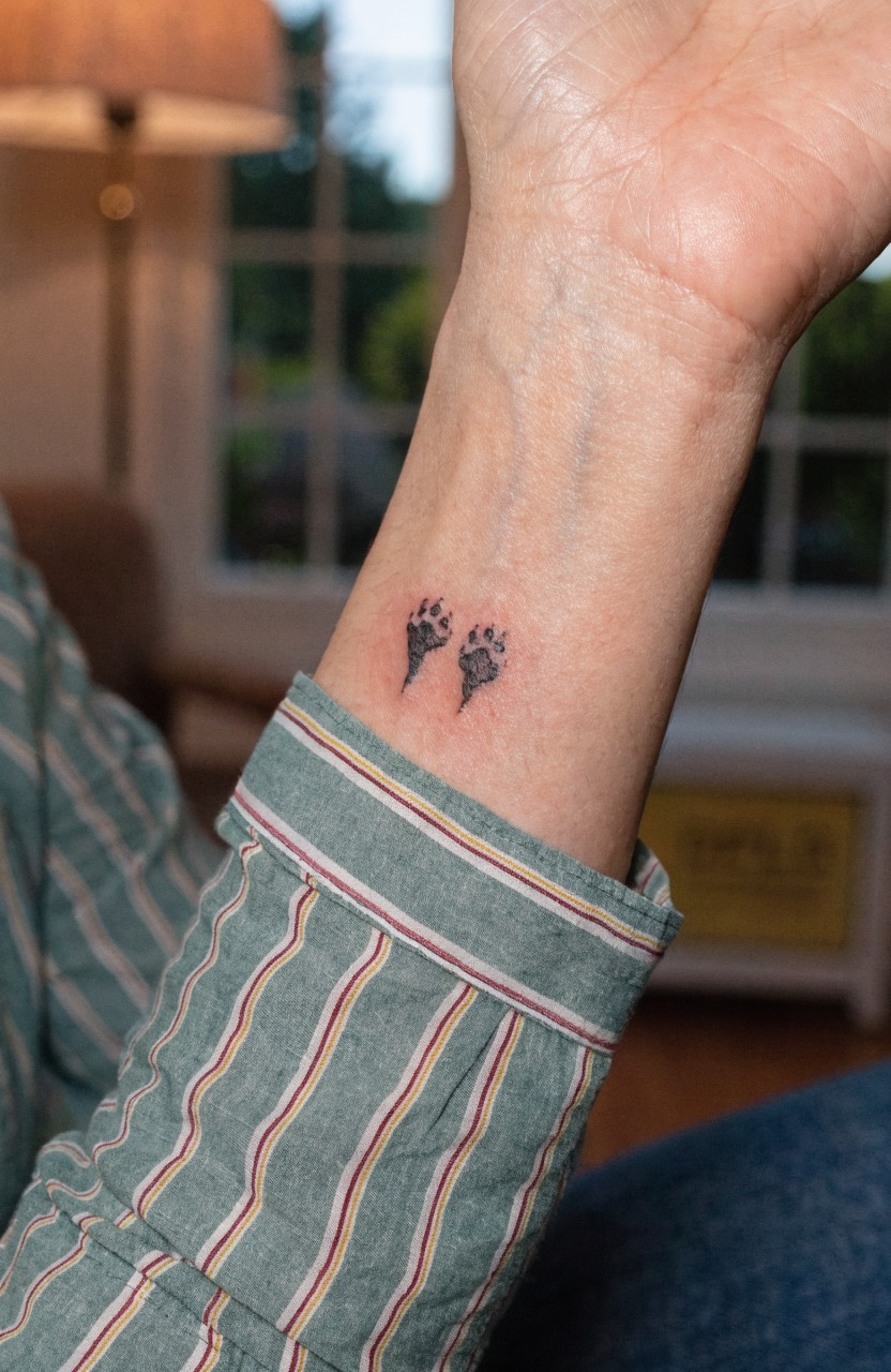 Two small fine line tiger paw print tattoos side by side on a person's inner wrist in black ink
