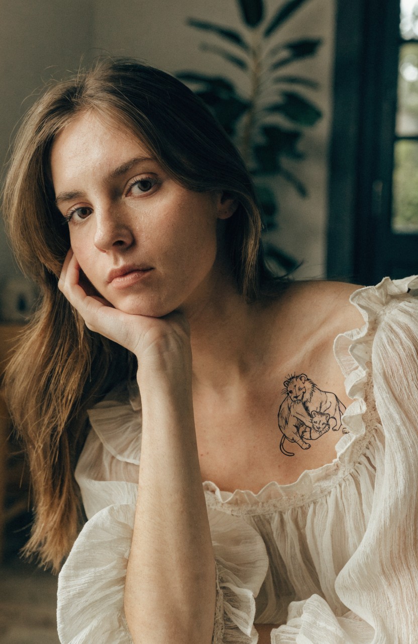 Black line art tattoo of mama lion embracing two cubs on a woman's upper chest