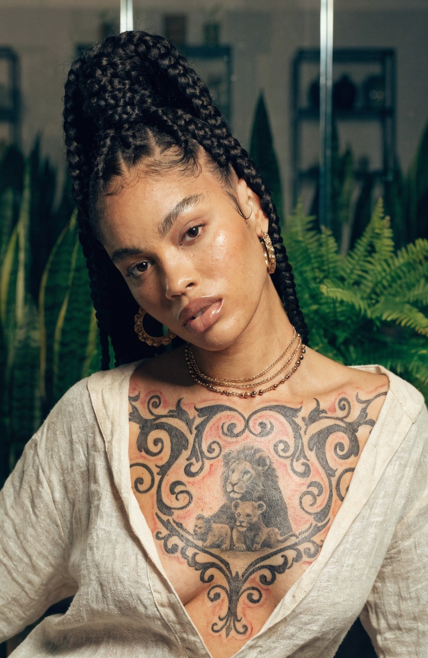 Black and grey realistic tattoo of lioness with cub in ornate filigree frame across woman's upper chest