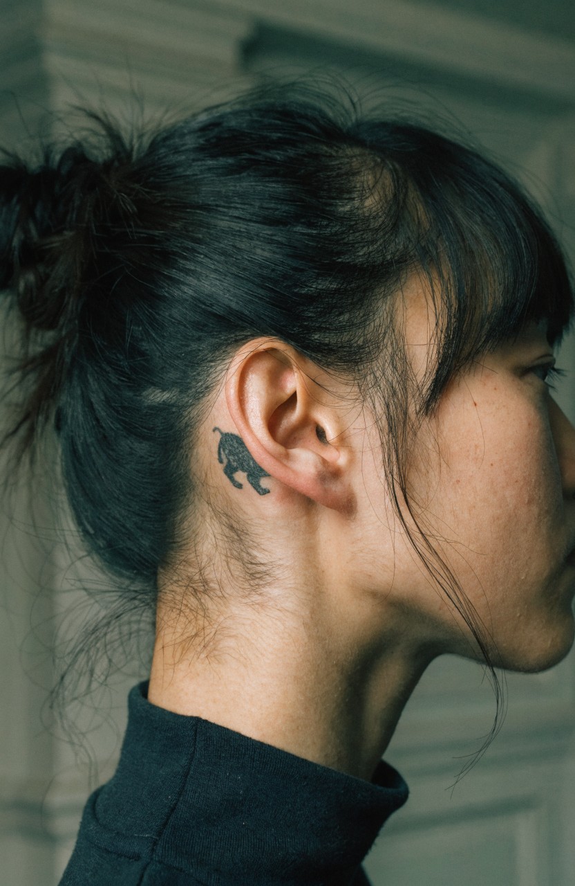 Black ink tiger head tattoo behind a woman's ear on the side of her neck