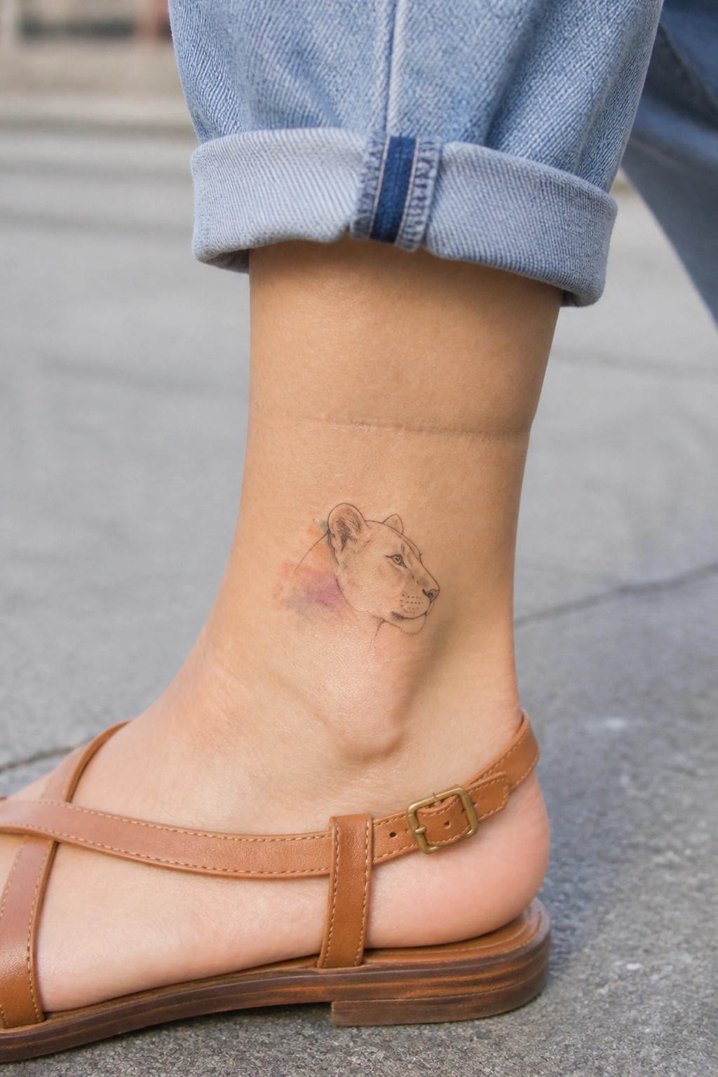 Small watercolor lioness head tattoo on the outer ankle in profile view with soft color accents.