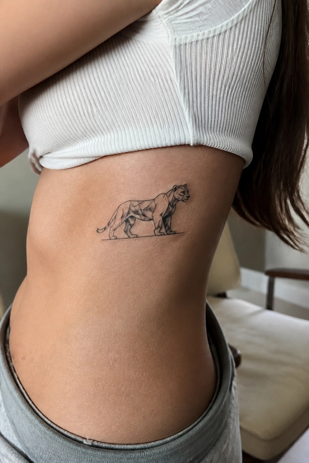 Small geometric lioness tattoo placed on the ribs in black ink with a thin base line underneath