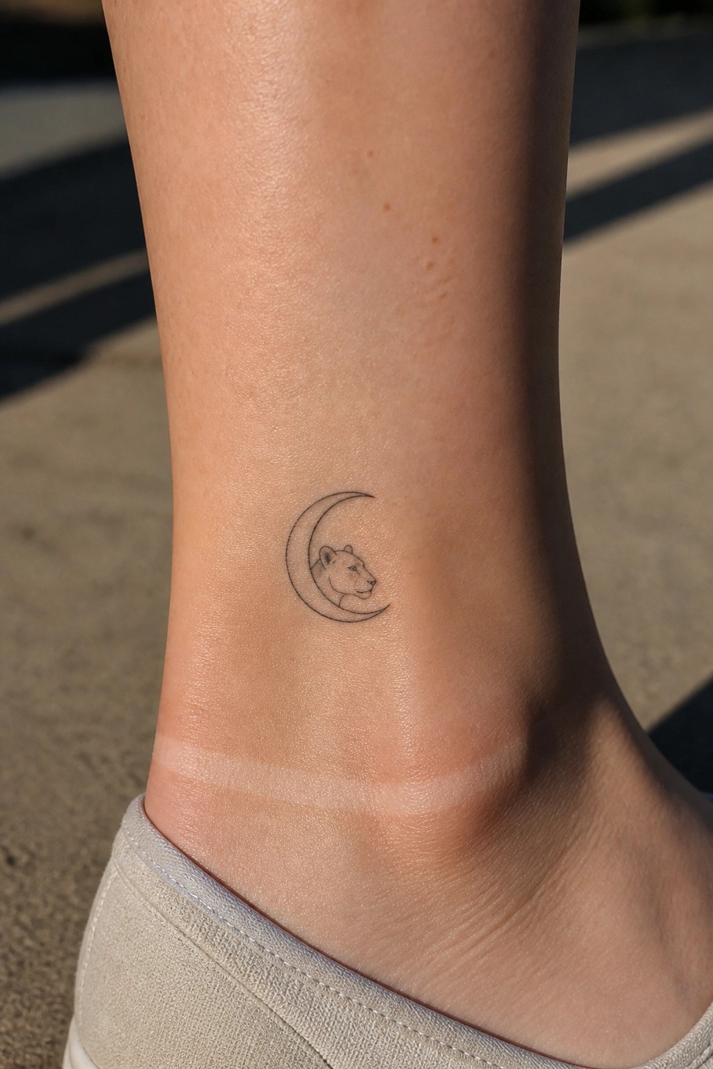 Crescent moon tattoo with lion head on light-skinned ankle above shoe.