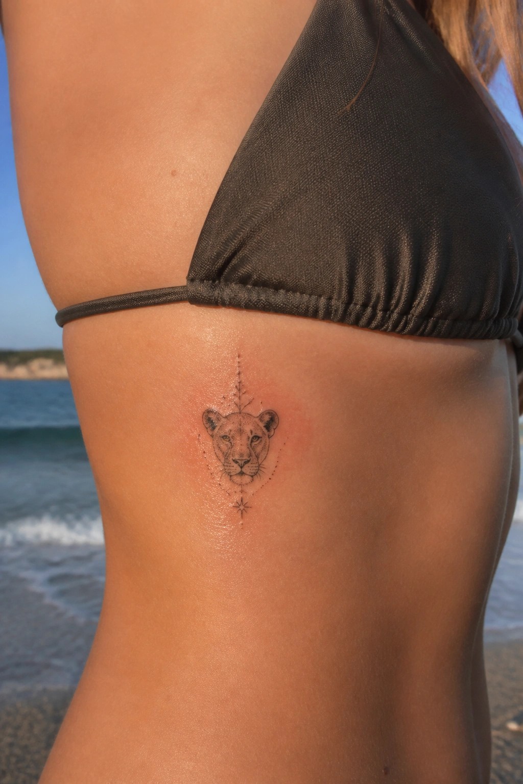 Small fine line lioness head tattoo on the ribs with dotted geometric details and a star accent