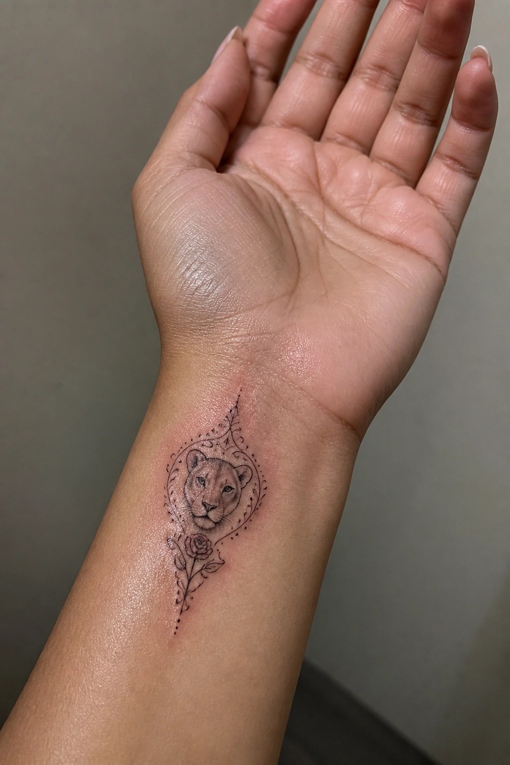Intricate black tattoo of a lioness and rose on inner wrist