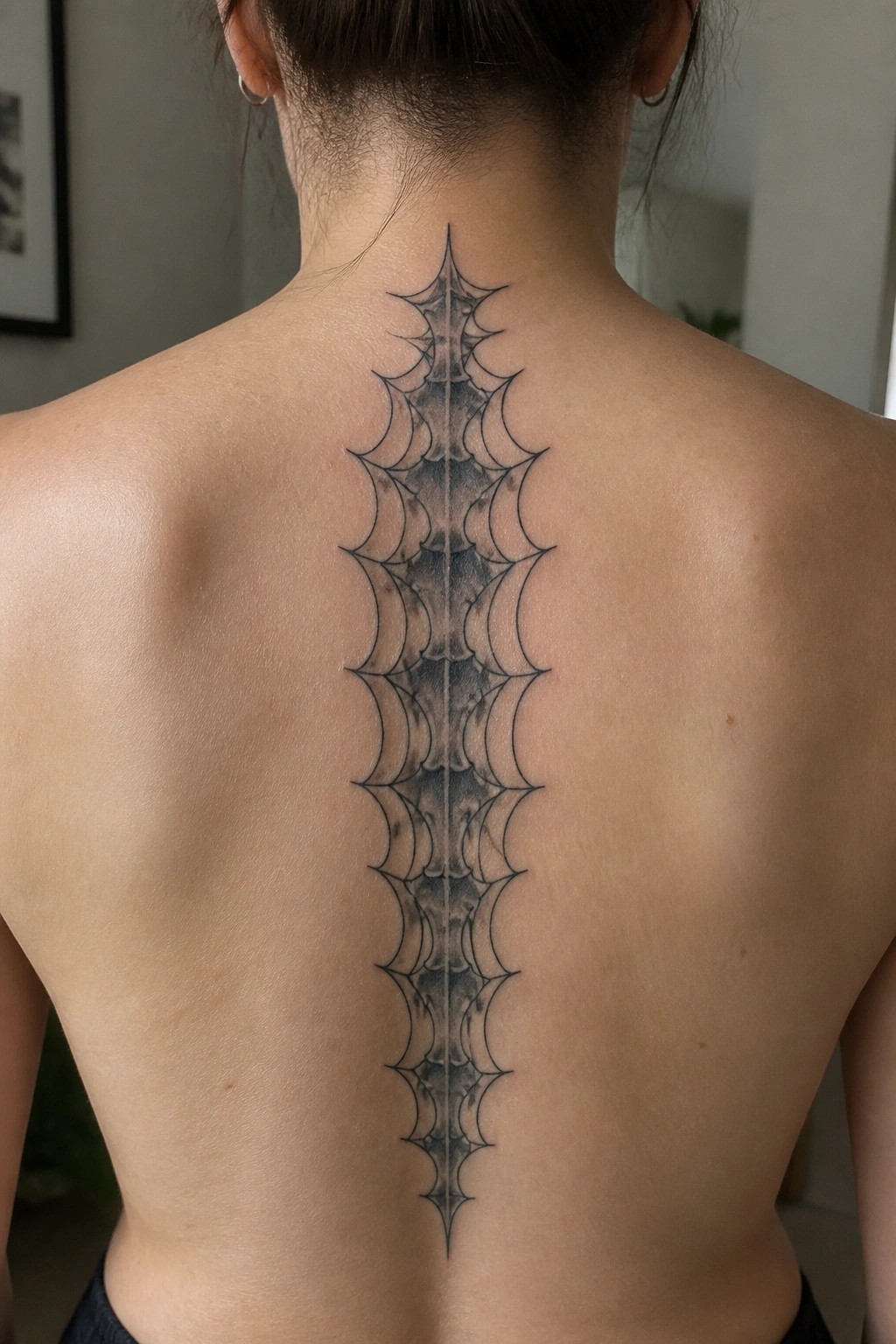 Black and grey spider web tattoo running vertically down the spine on a person's back with bold lines and light shading.
