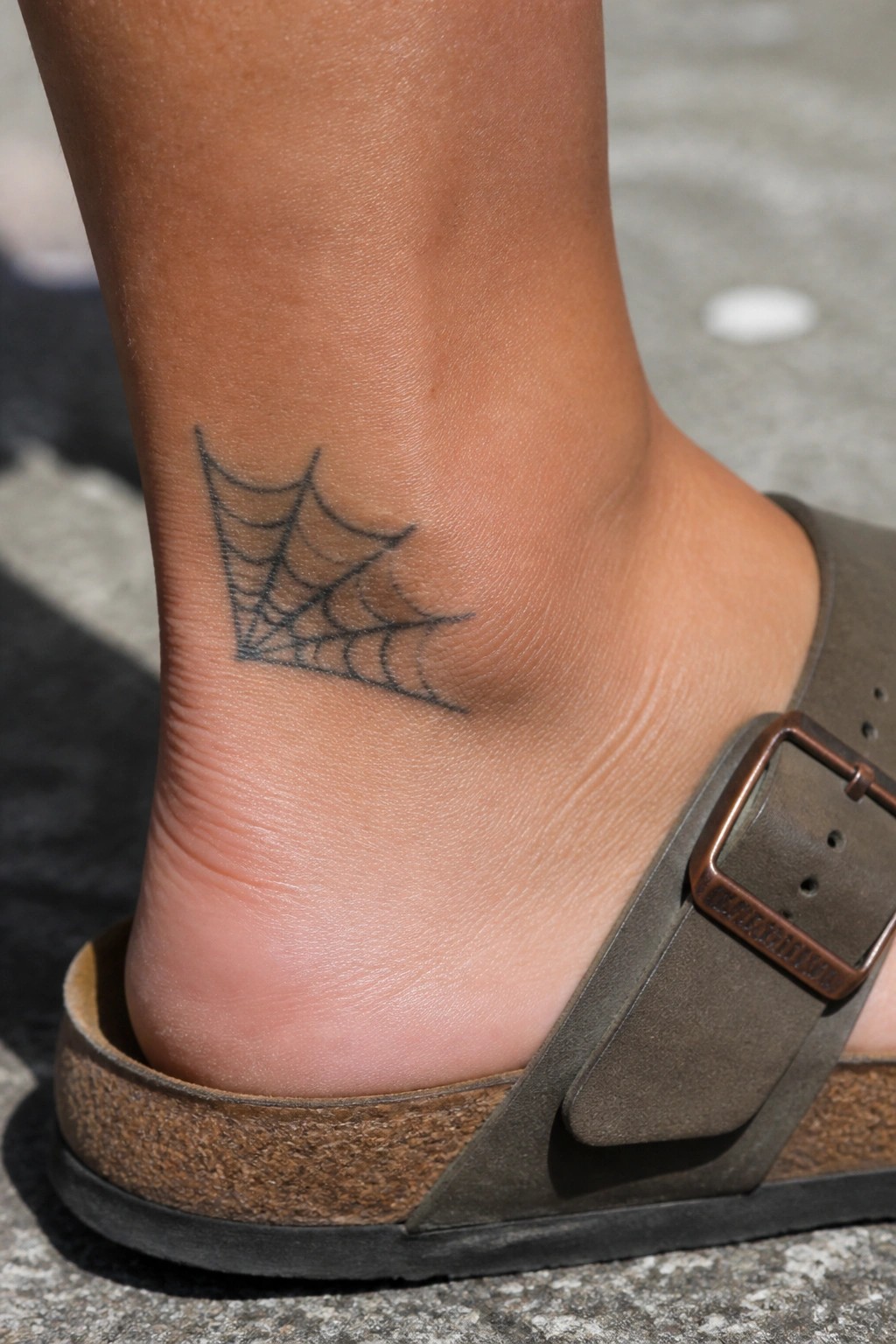 Traditional spider web tattoo on the ankle with bold black lines.