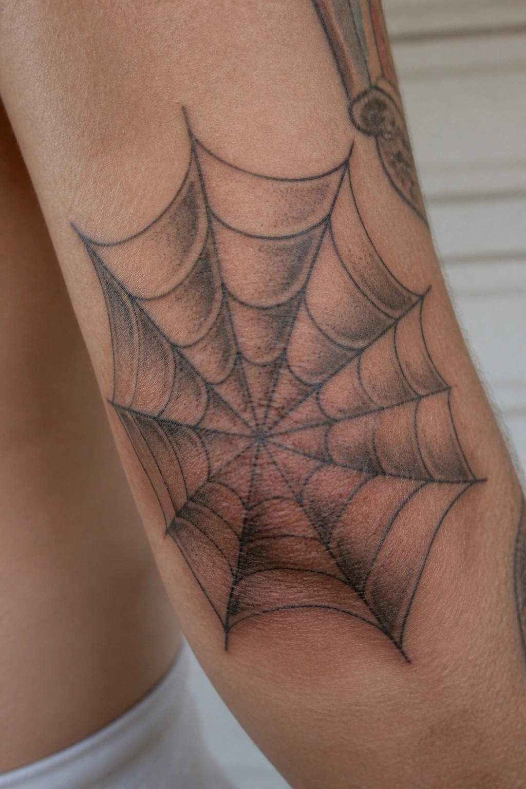 Black spider web tattoo with shading on a person's forearm skin
