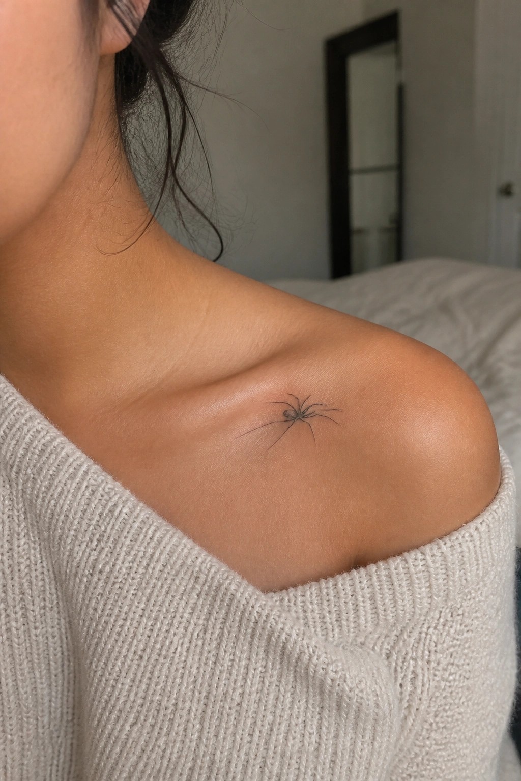 Woman's shoulder with small spider tattoo under off-shoulder cream sweater