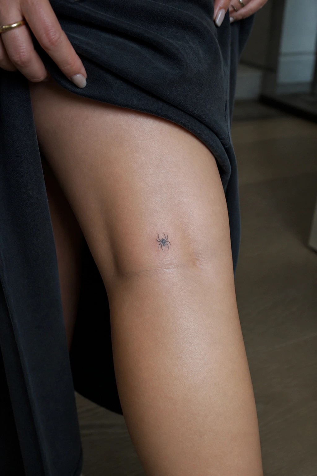 Small minimalist spider tattoo in clean black ink on a woman's upper thigh