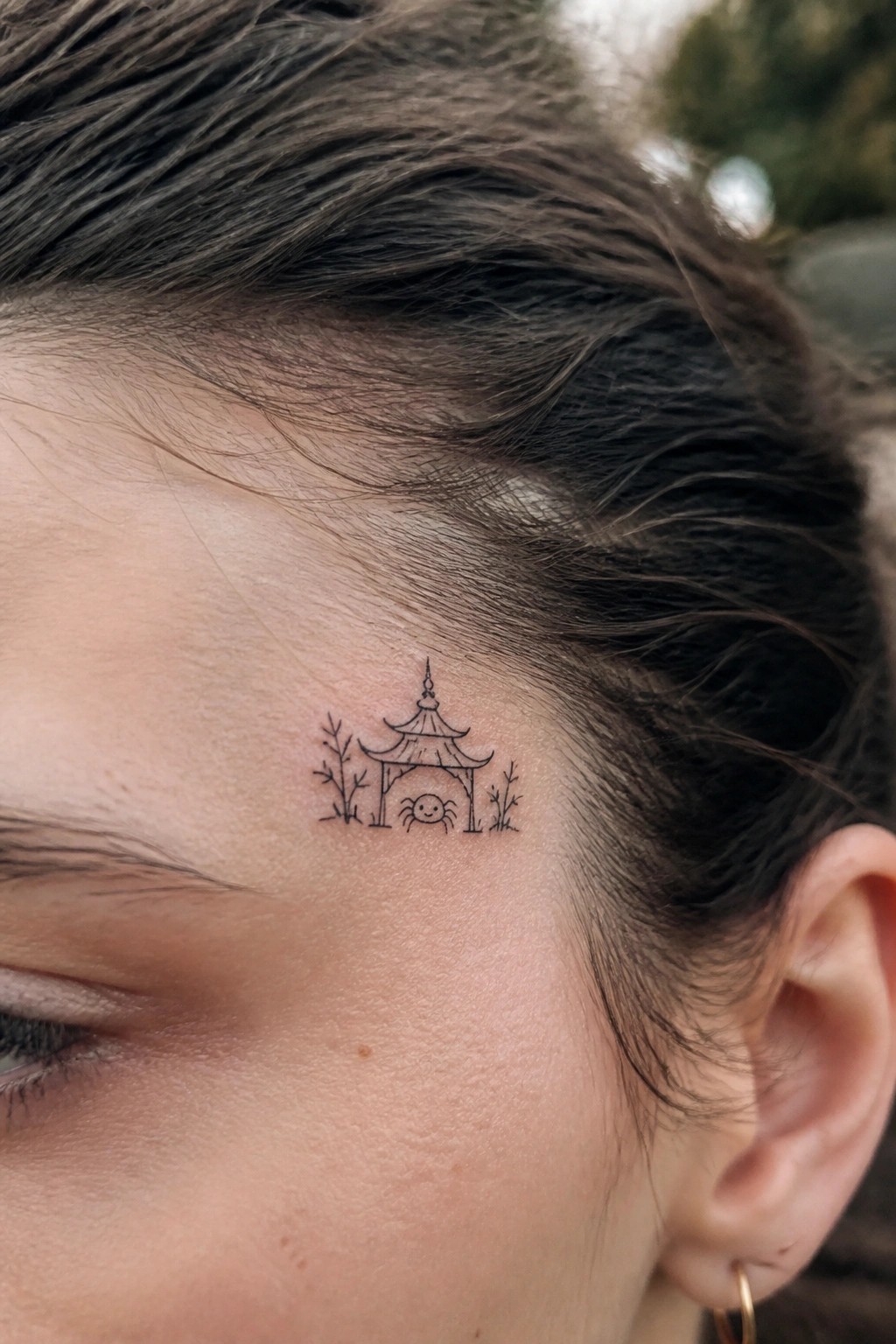 Fine-line tattoo of pagoda with smiling spider on temple near hairline