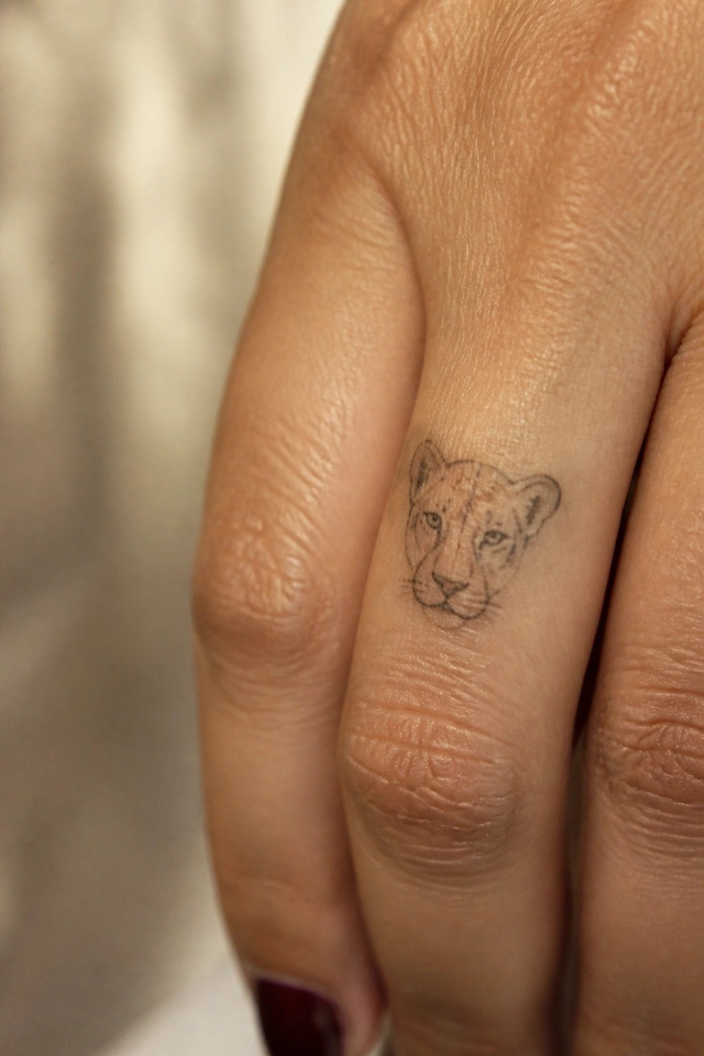Small lion face tattoo on side of finger with dark nail polish