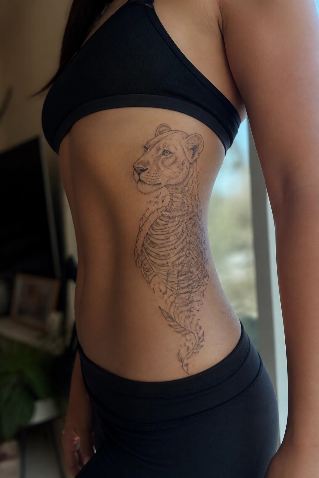 Woman's side torso in black activewear with lioness skeleton tattoo.