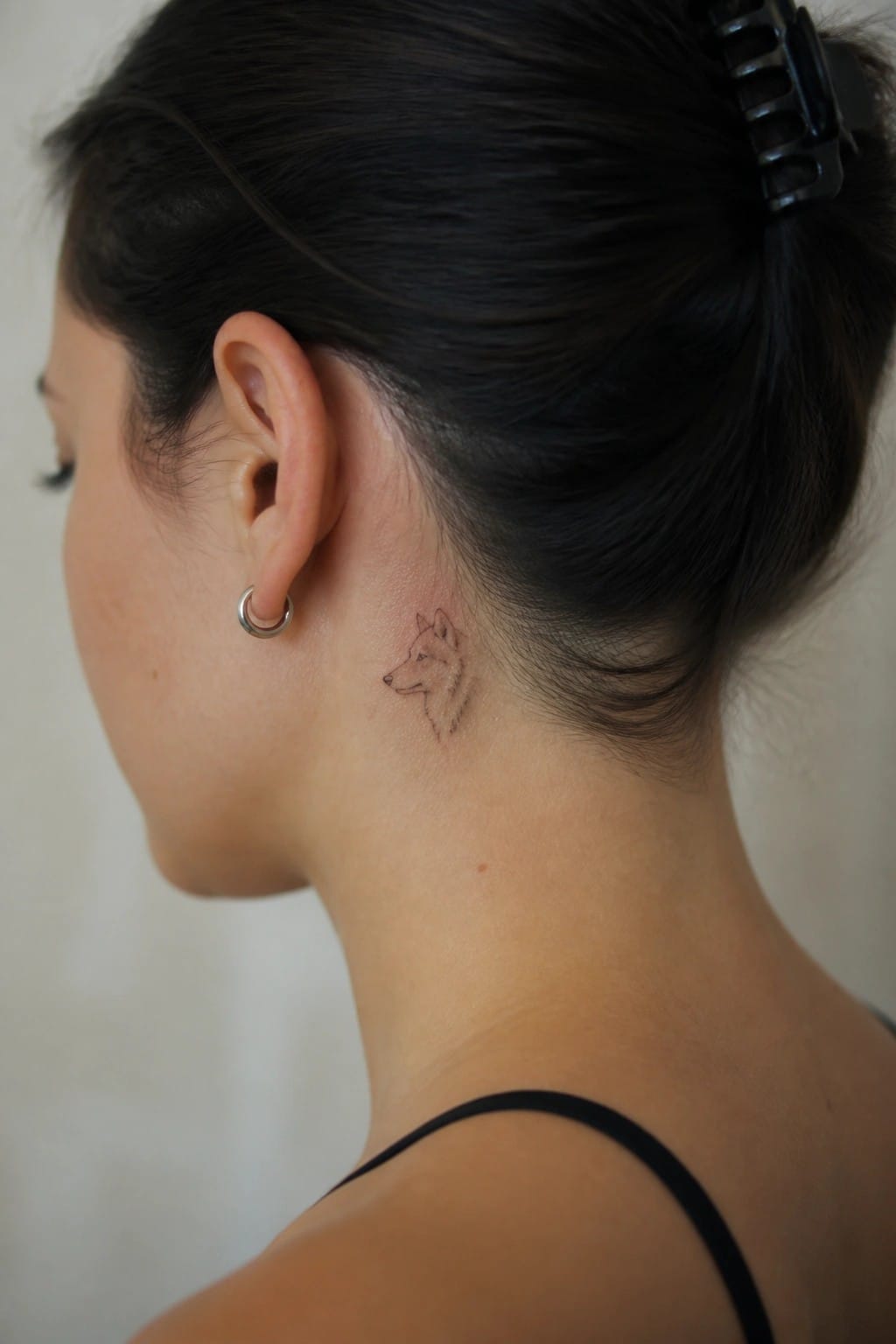 Woman with dark hair in bun and small wolf tattoo on neck