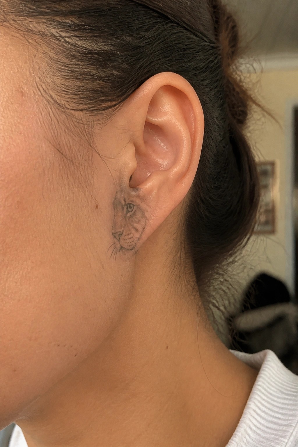 Lion tattoo behind a woman's ear, dark hair pulled back in white top.