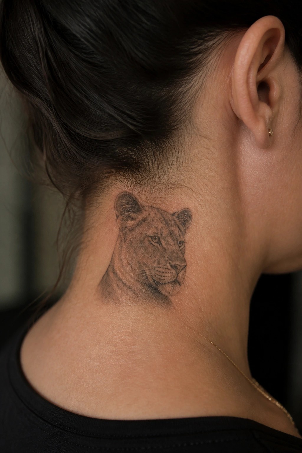 Realistic black and gray lioness head tattoo in profile on the back of a woman's neck below the hairline.