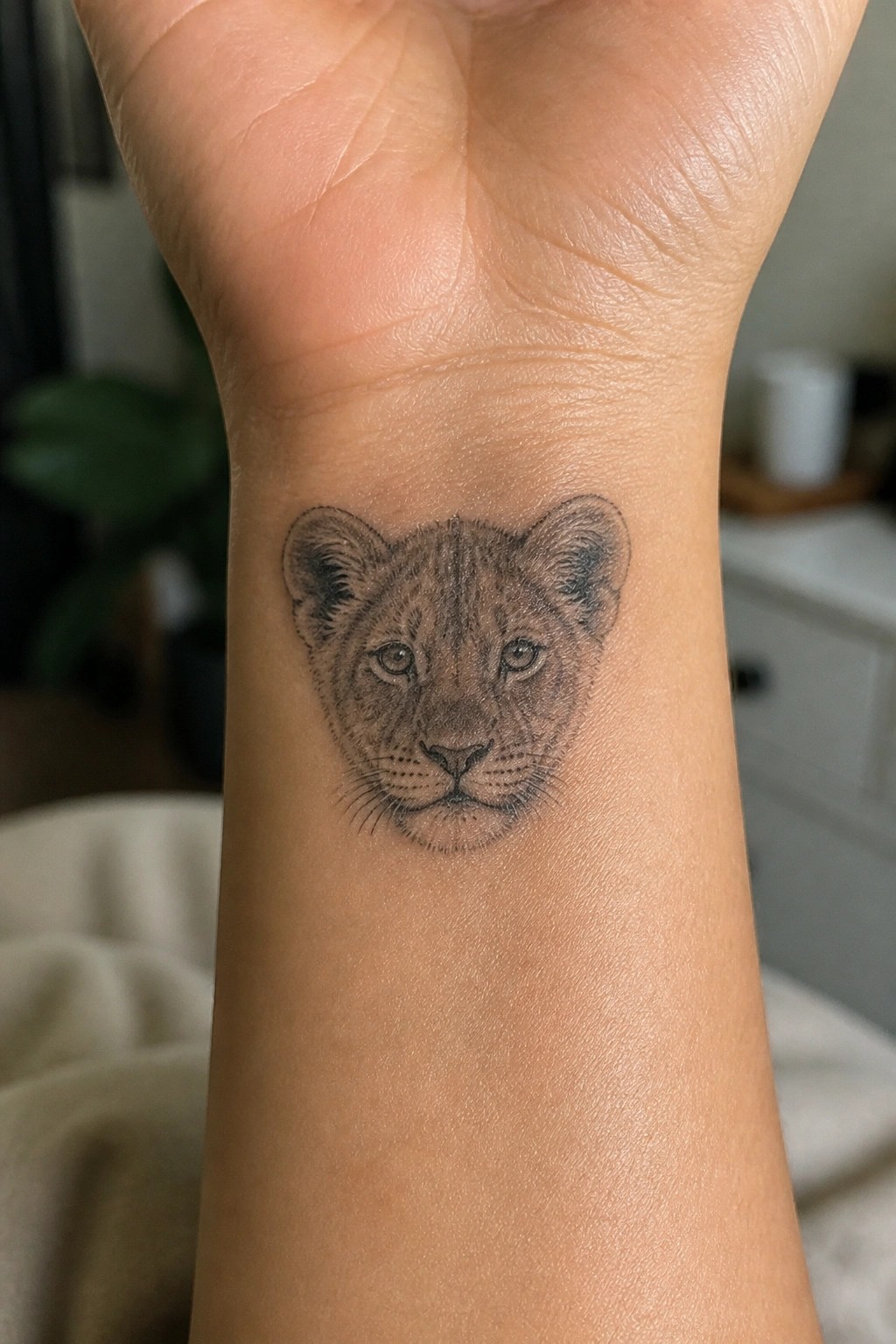 Realistic black and gray lion cub tattoo on a person's inner wrist