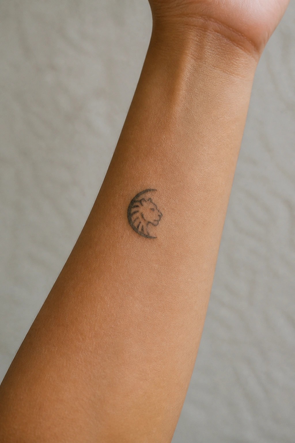 Close-up of a black lion-and-crescent-moon tattoo on a light-brown forearm.