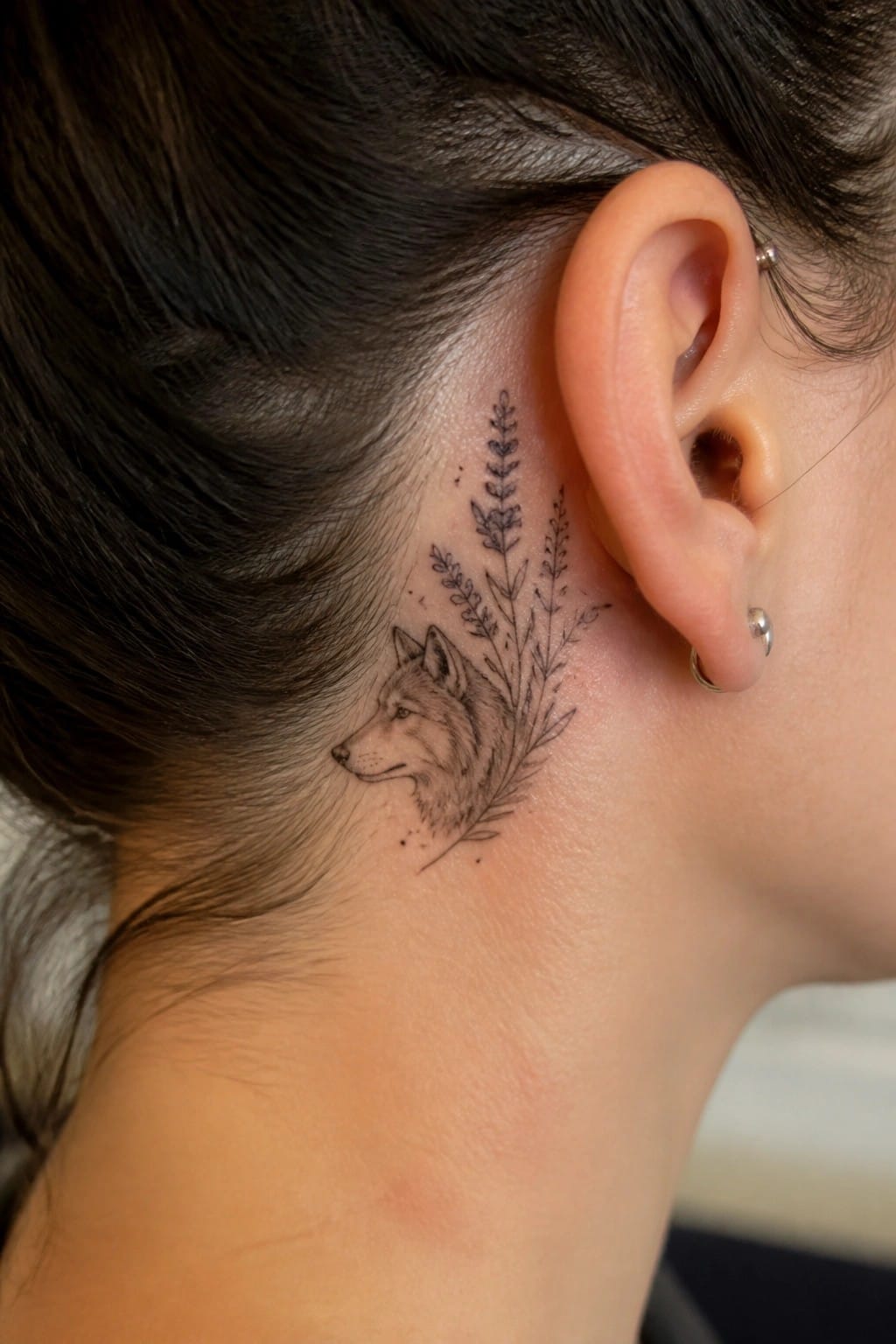 Fine line wolf head tattoo with surrounding florals placed behind a woman's ear on the neck