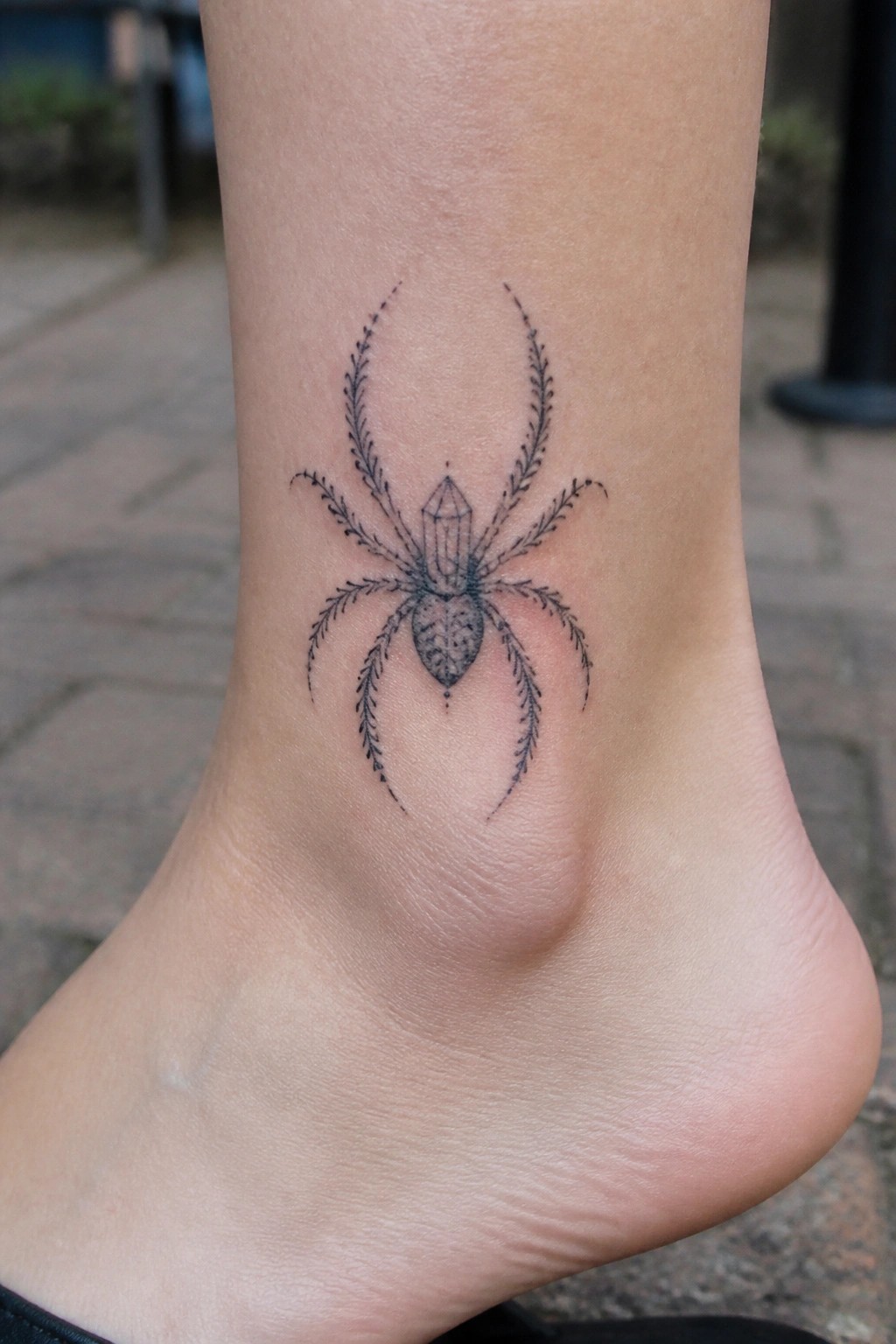 Black spider tattoo with crystal body and feathery legs on ankle